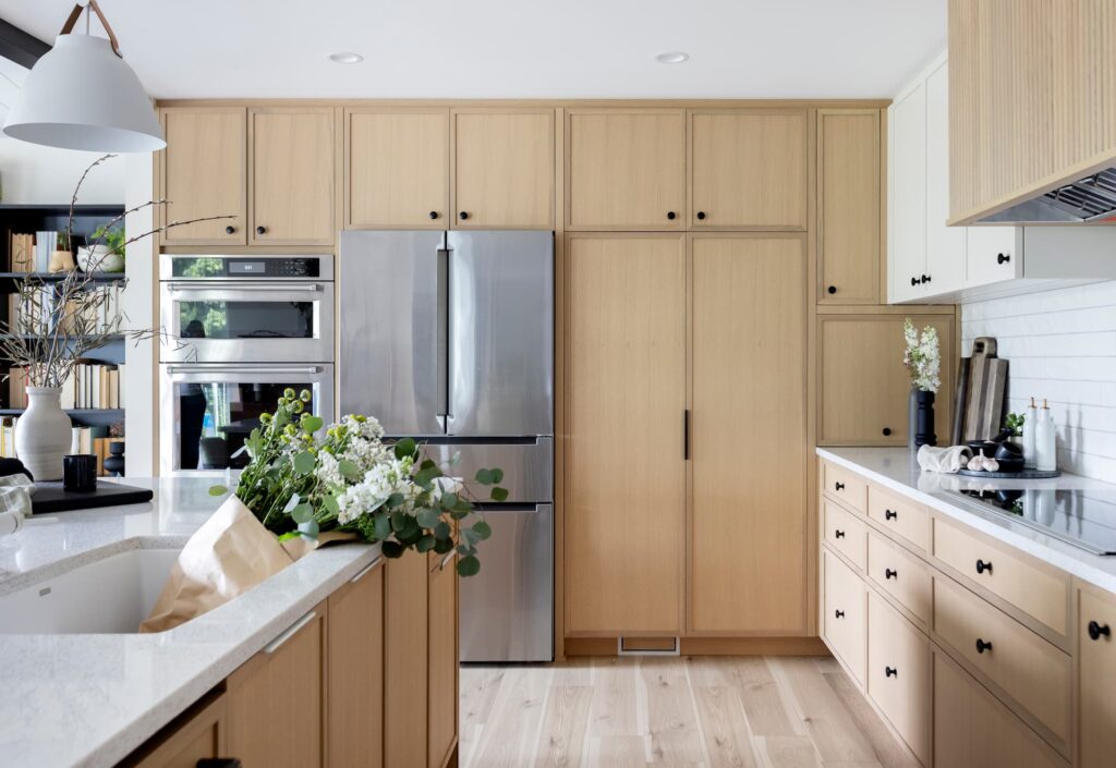 Bright modern kitchen renovation with light wood cabinetry, built-in stainless steel appliances, and a spacious island accented by fresh florals