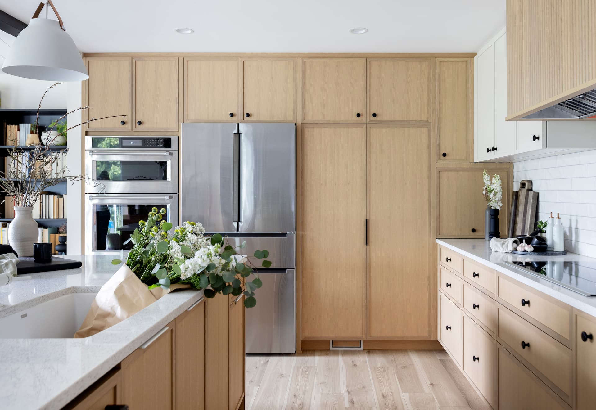 Bright modern kitchen renovation with light wood cabinetry, built-in stainless steel appliances, and a spacious island accented by fresh florals