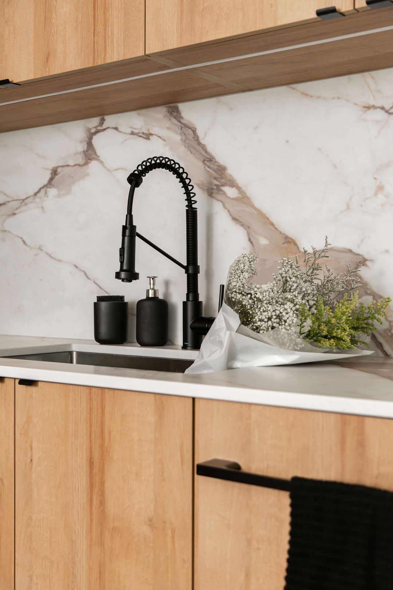 Elegant kitchen renovation sink setup featuring a matte black faucet, wood cabinetry, and a striking marble backsplash