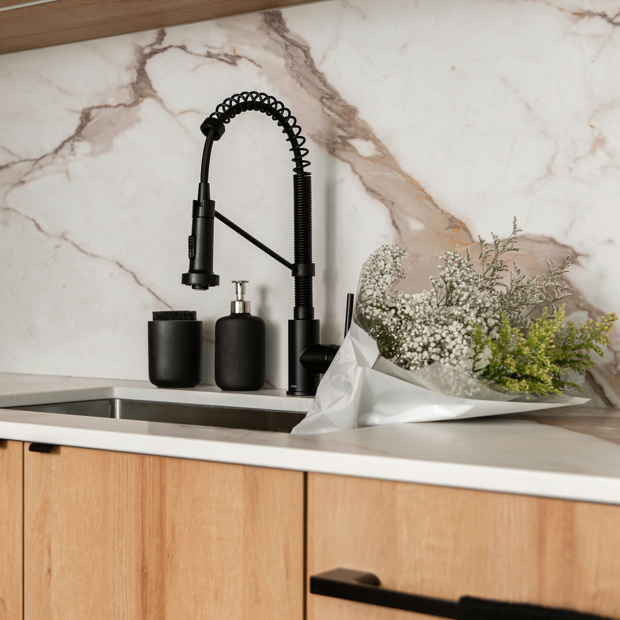 Elegant kitchen renovation sink setup featuring a matte black faucet, wood cabinetry, and a striking marble backsplash