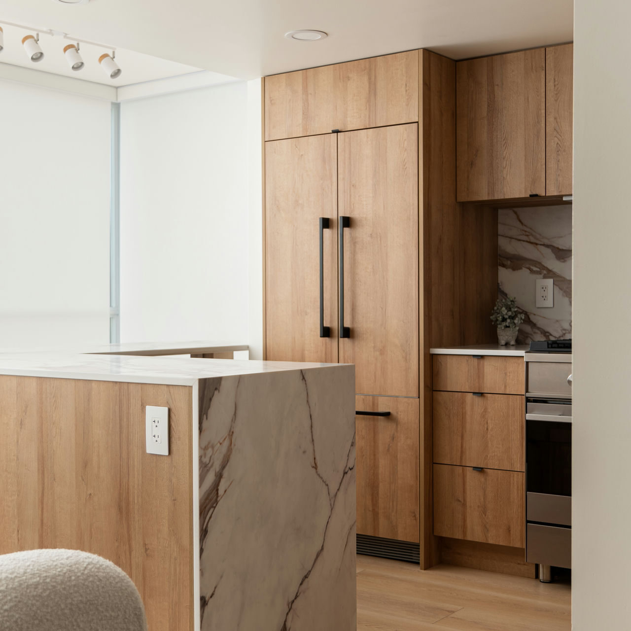 Modern kitchen renovation with sleek wood cabinetry, integrated appliances, and a marble waterfall island for a clean, contemporary look